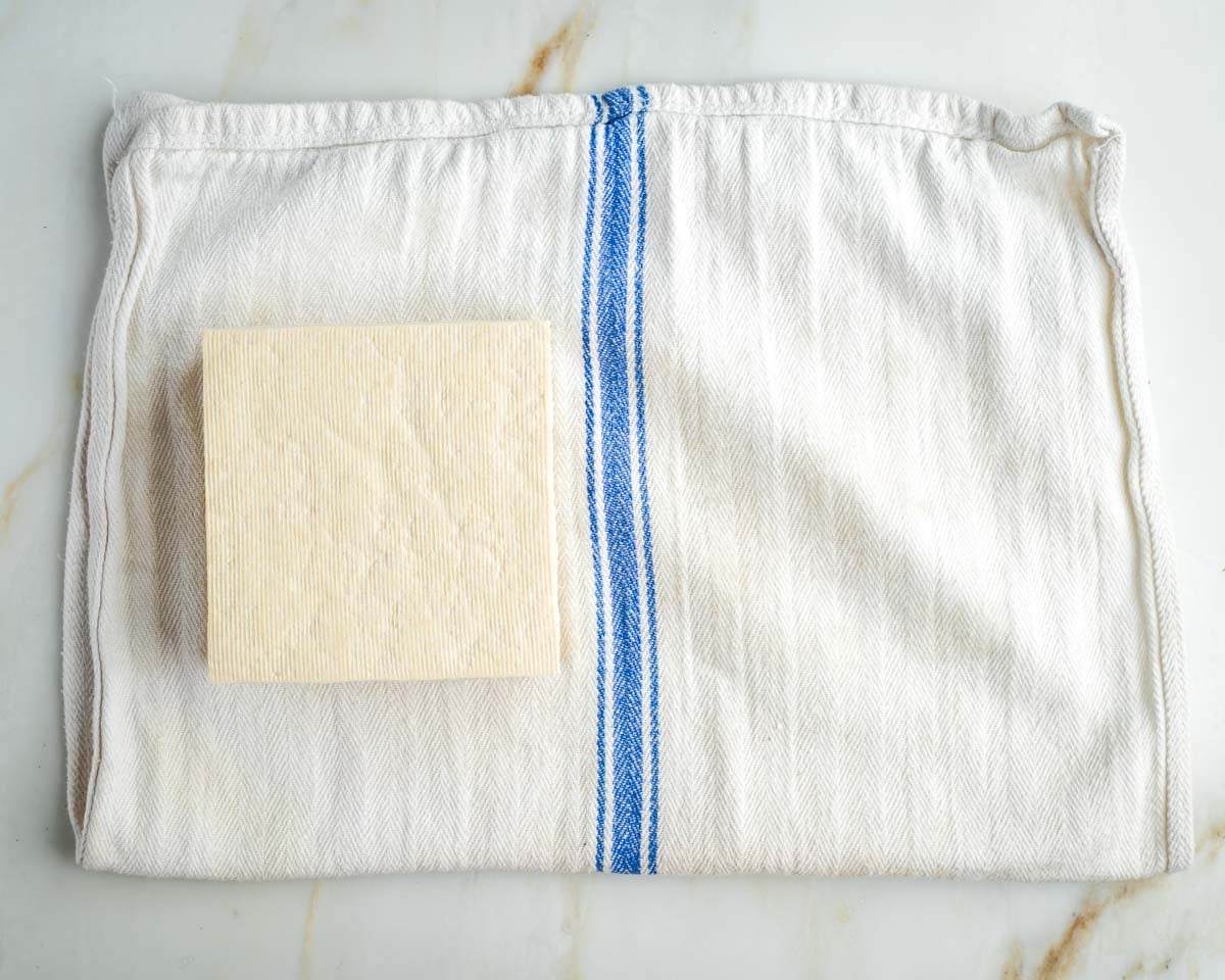 Block of tofu on a white kitchen towel with blue stripe.
