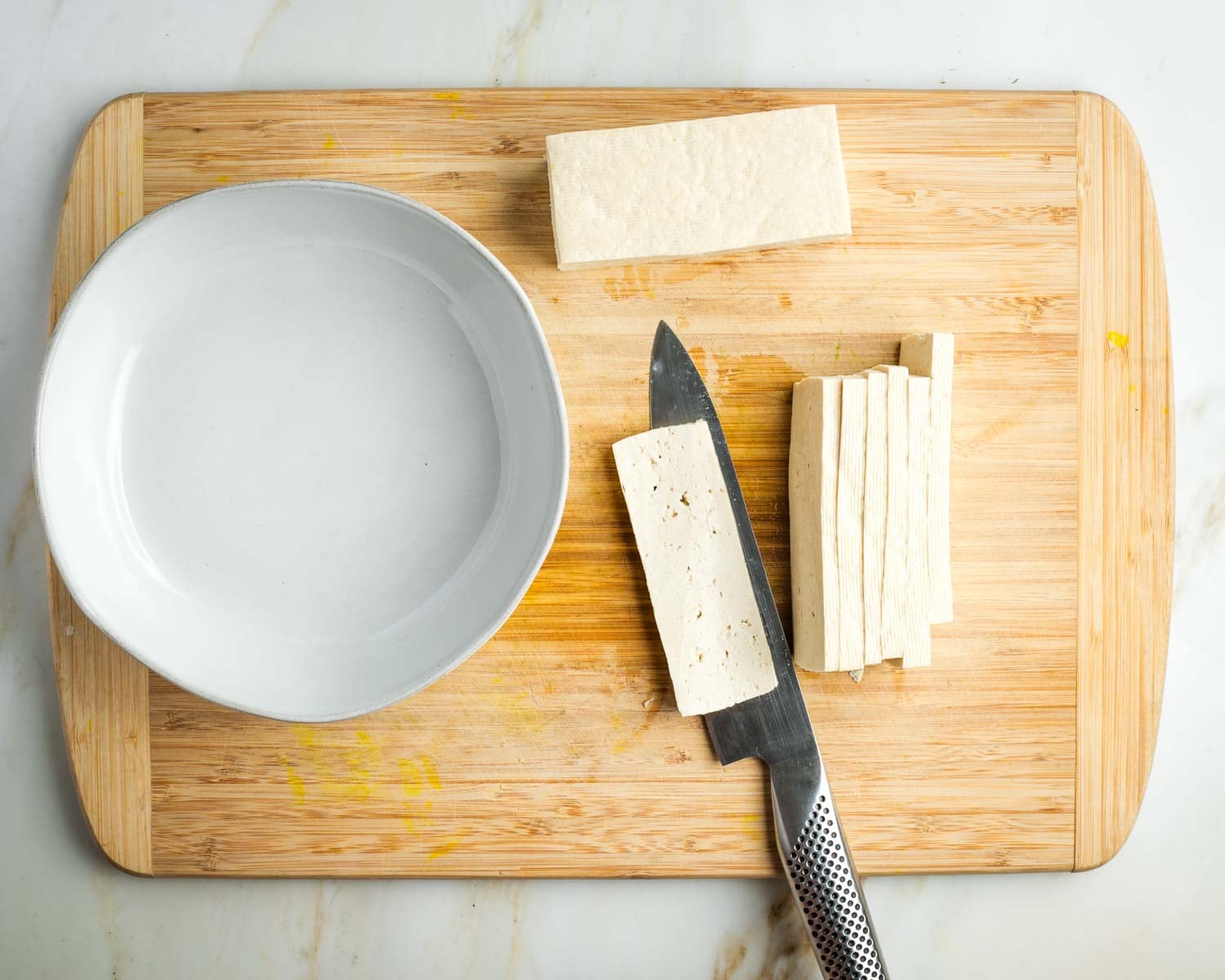 Cutting half a block of tofu into thin slices.