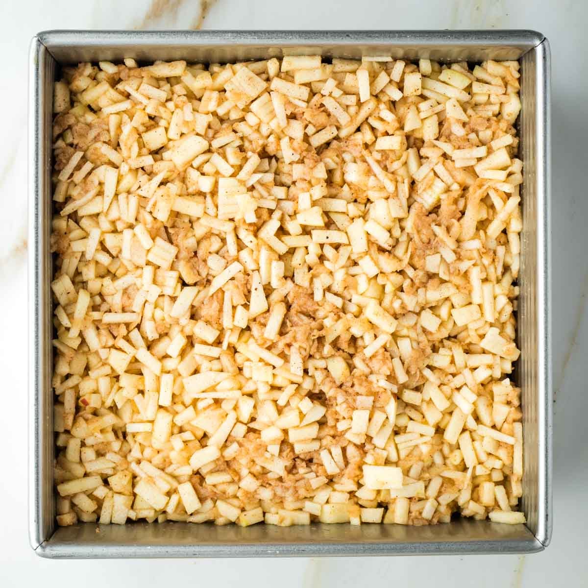 Small pieces of apples and spices in a square pan on top of a piece of pie dough.