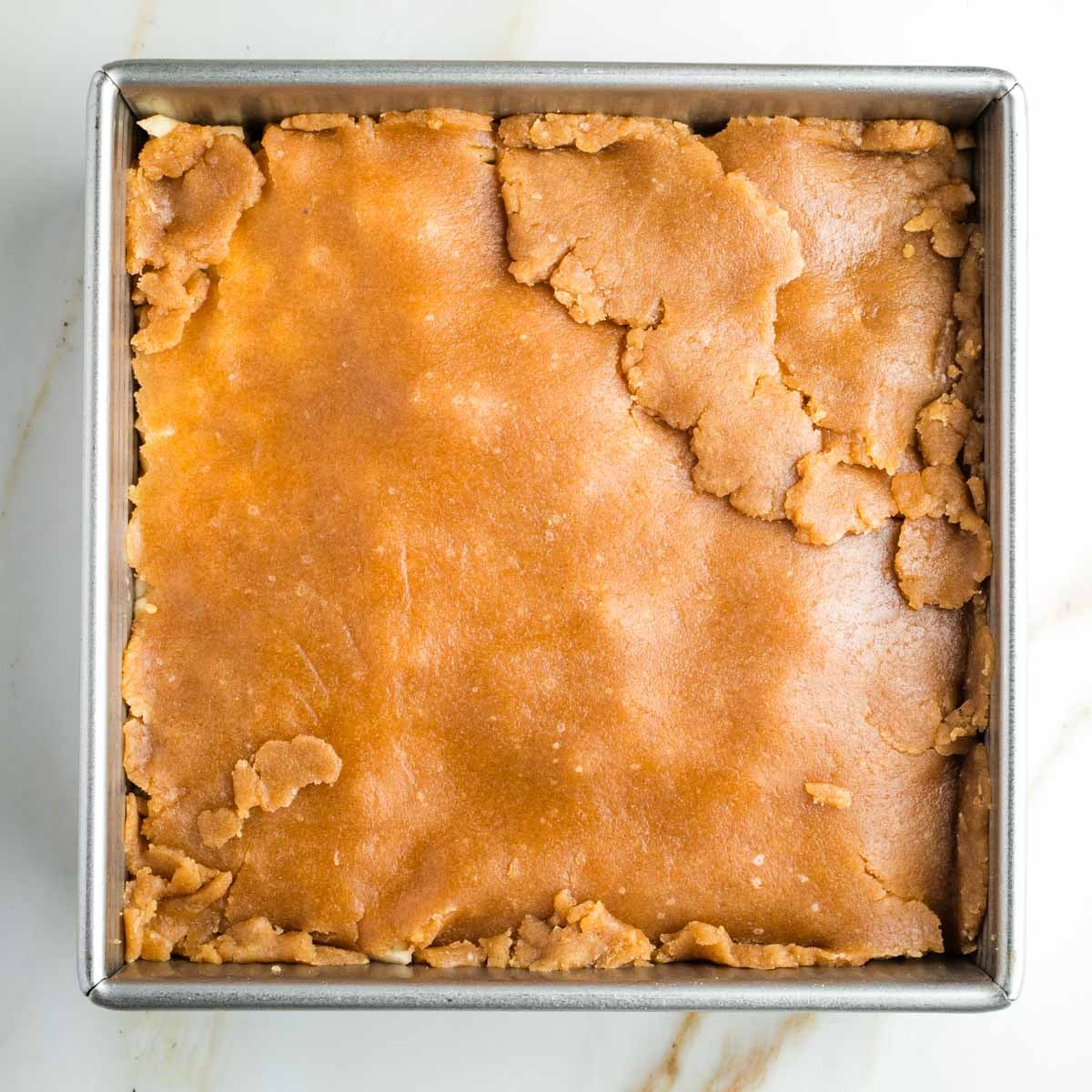 Pie dough pieced together, covering apples in a square pan.