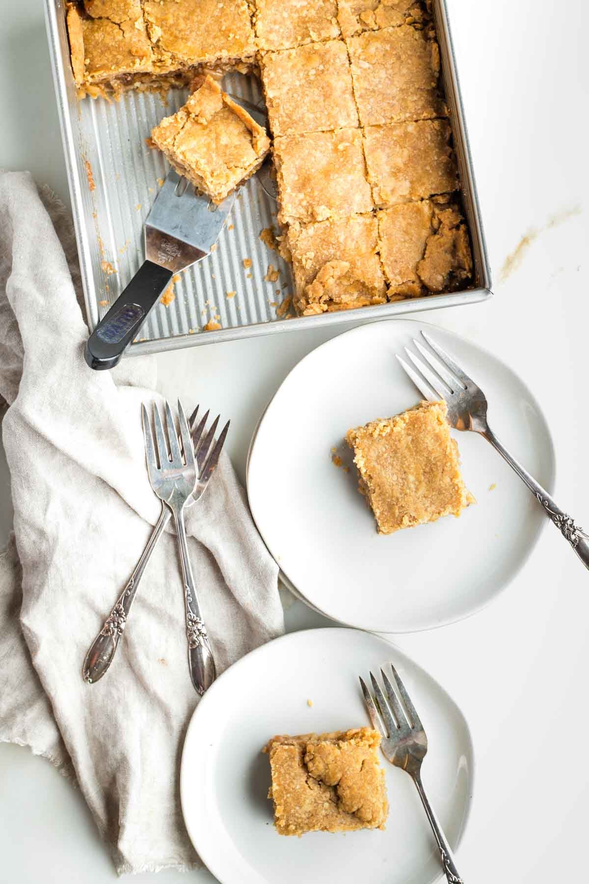 Apple pie bars on plates with forks and in the square brownie pan being served.