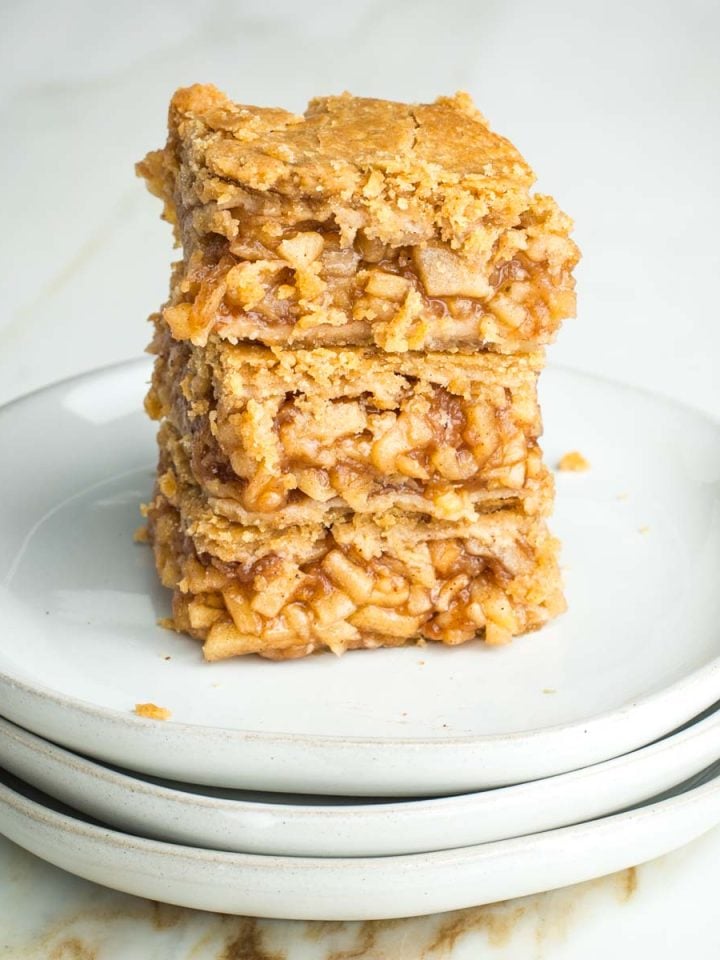 Stack of three apple pie bars with tiny pieces of apples in a thick jammy sauce, nestled between layers of flakey vegan crust.
