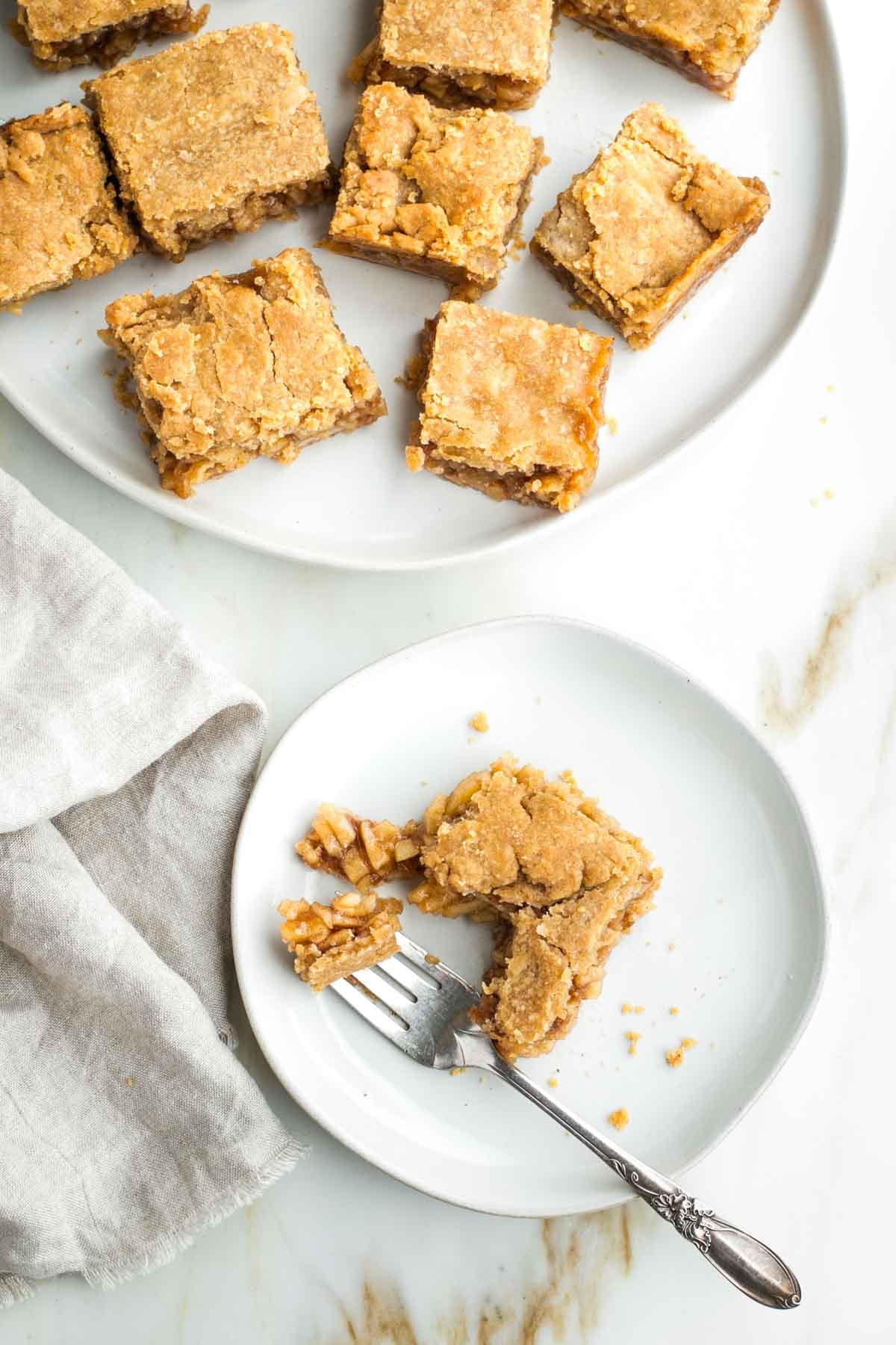 Apple pie bars, and one on a plate being eaten with a fork, showing the inside pieces of apples.