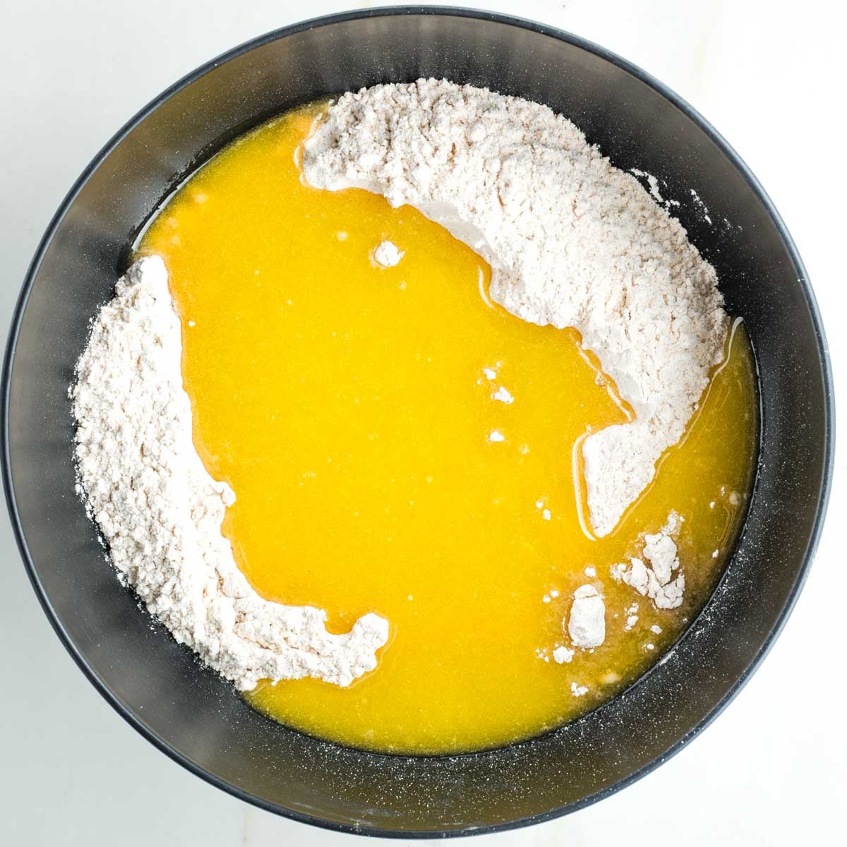 Flour in a black bowl, with yellow liquid poured on top.