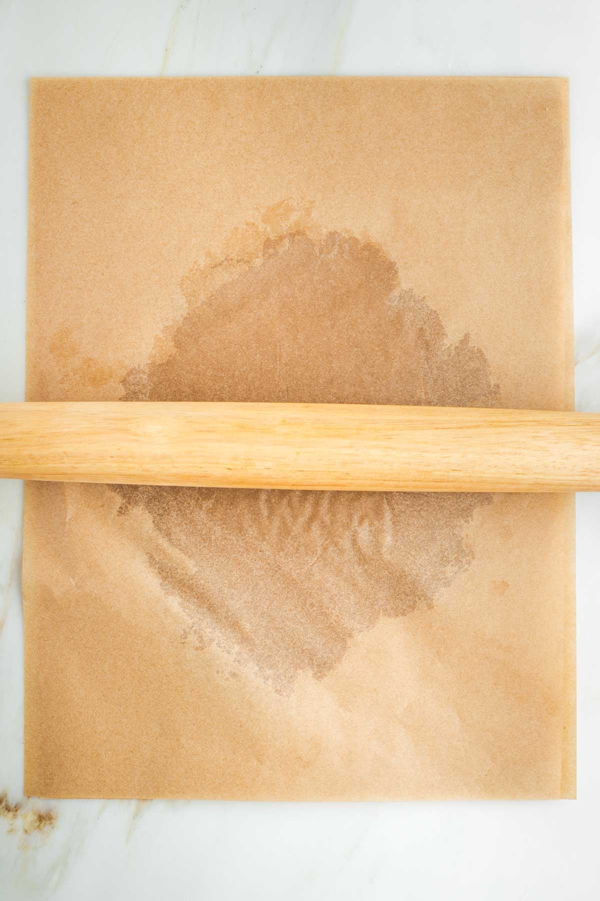 Using a rolling pin to roll out pie dough into a large circle, between two pieces of parchment paper.