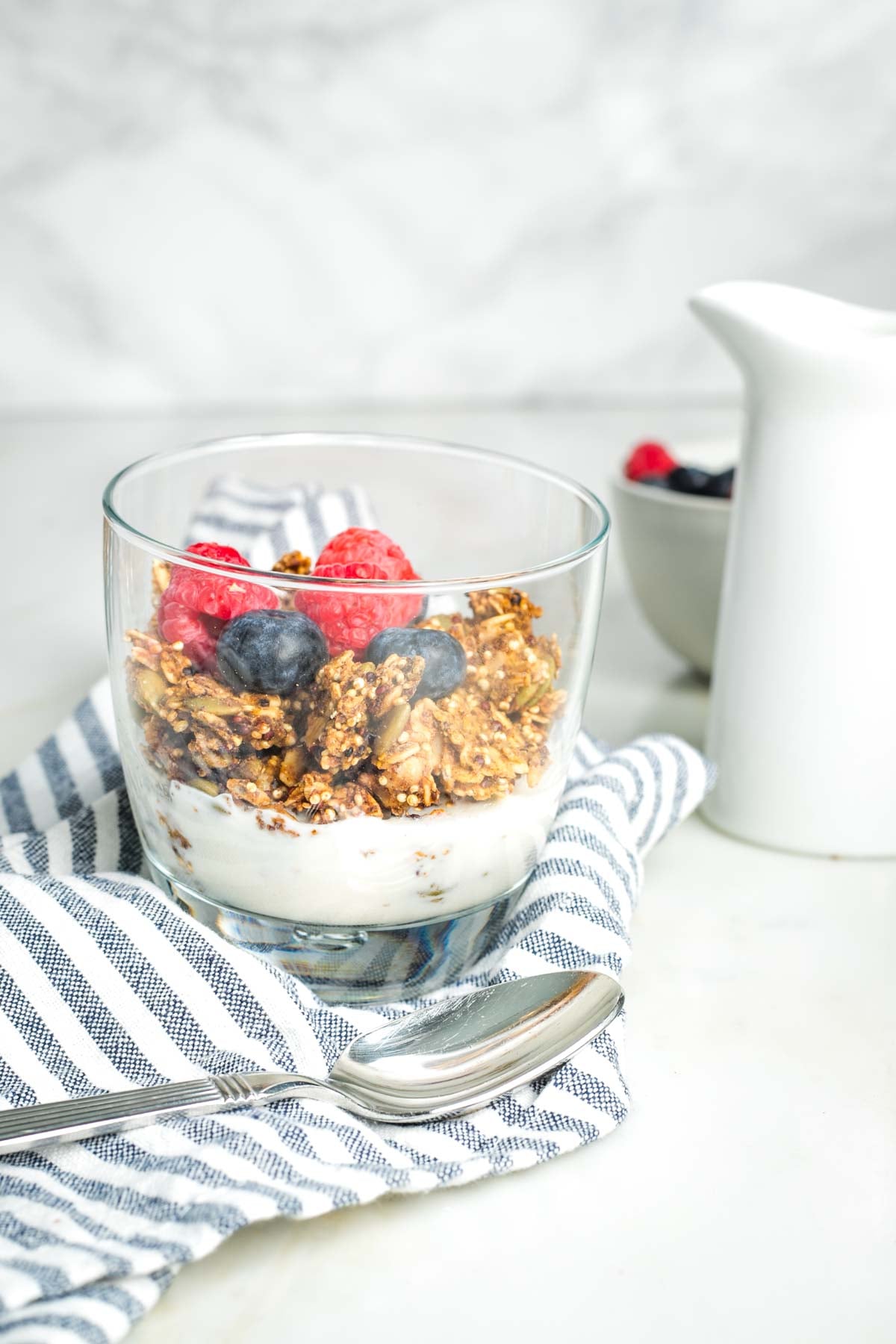 Glass with granola and milk, topped with fresh raspberries and blueberries.