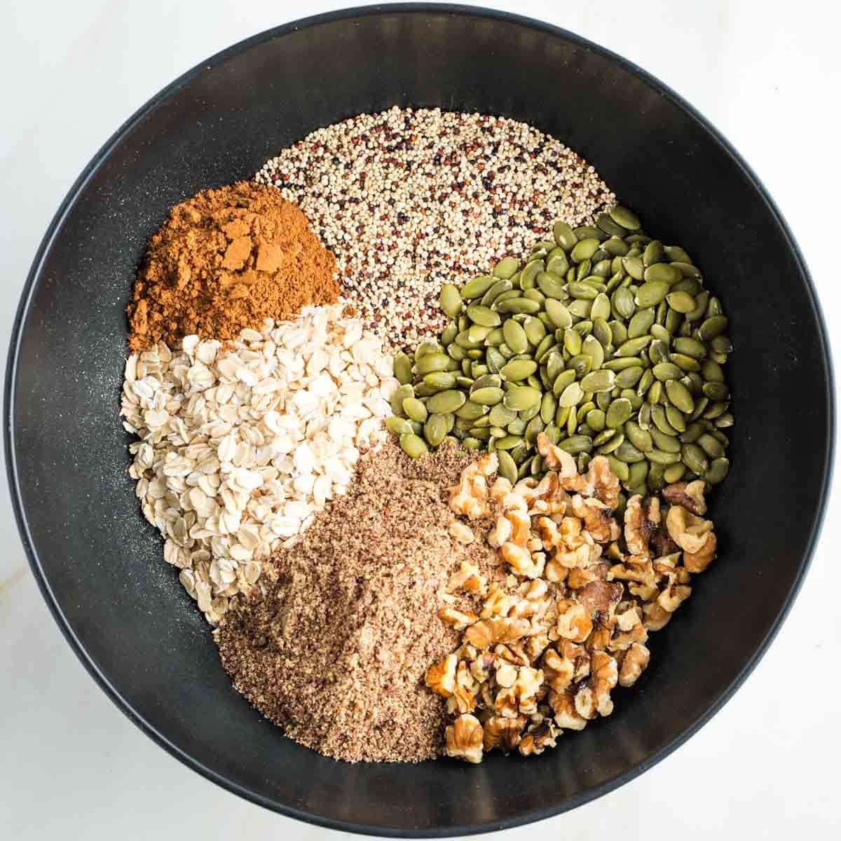 Sections in a bowl of pumpkin seeds, oats, walnuts, ground flax, dry quinoa, pumpkin pie spice.