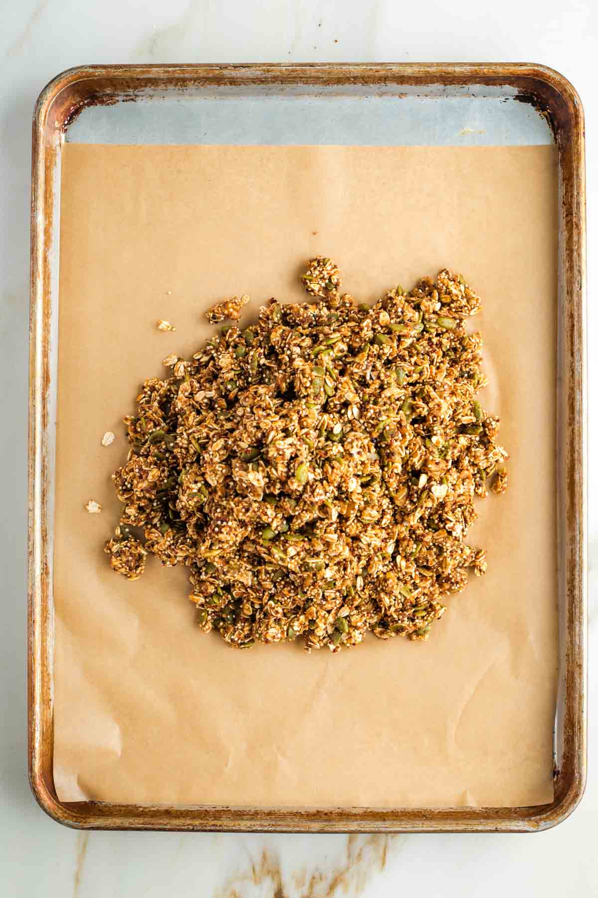 Wet, unbaked, granola mixture transferred in a heap onto a baking tray.
