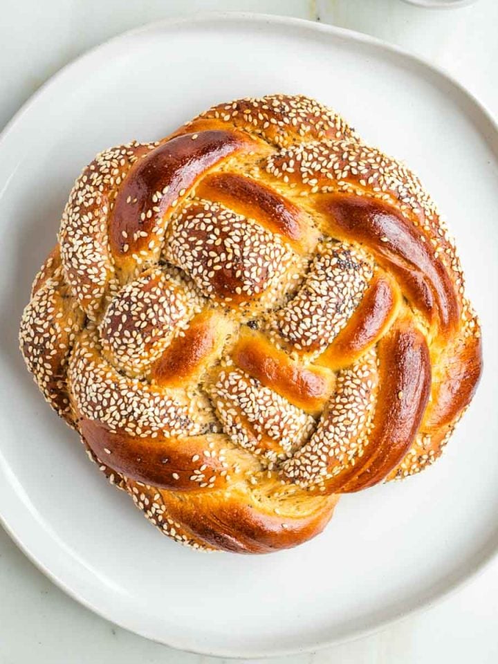 Round, braided challah, some strands with sesame and poppy seeds.