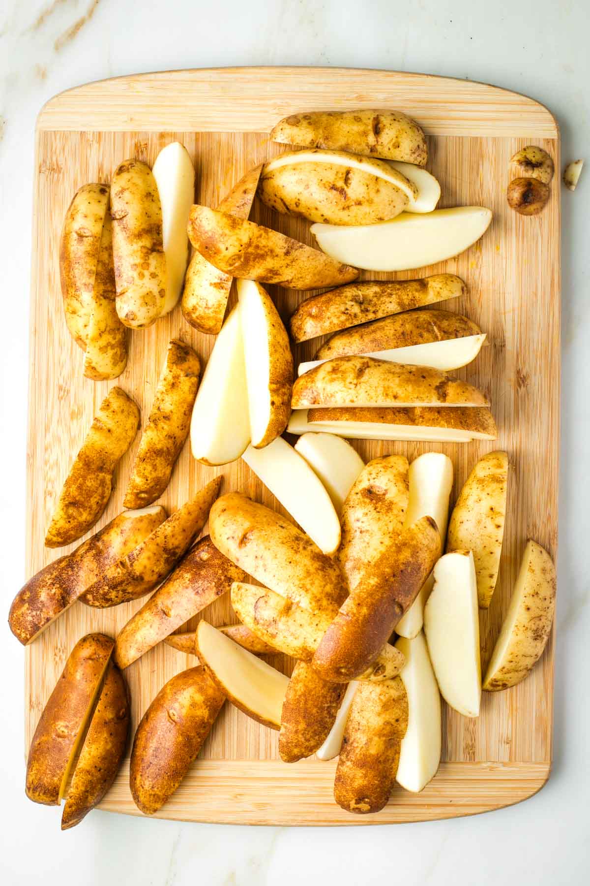 Russet potatoes cut into quarters lengthwise on a wooden board. 