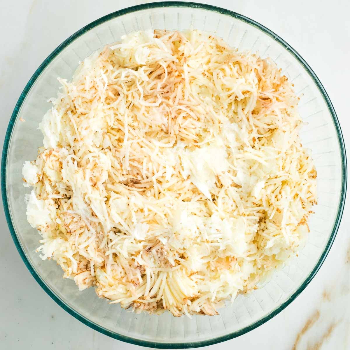 Thinly shredded unpeeled potatoes and onions in a large glass bowl.