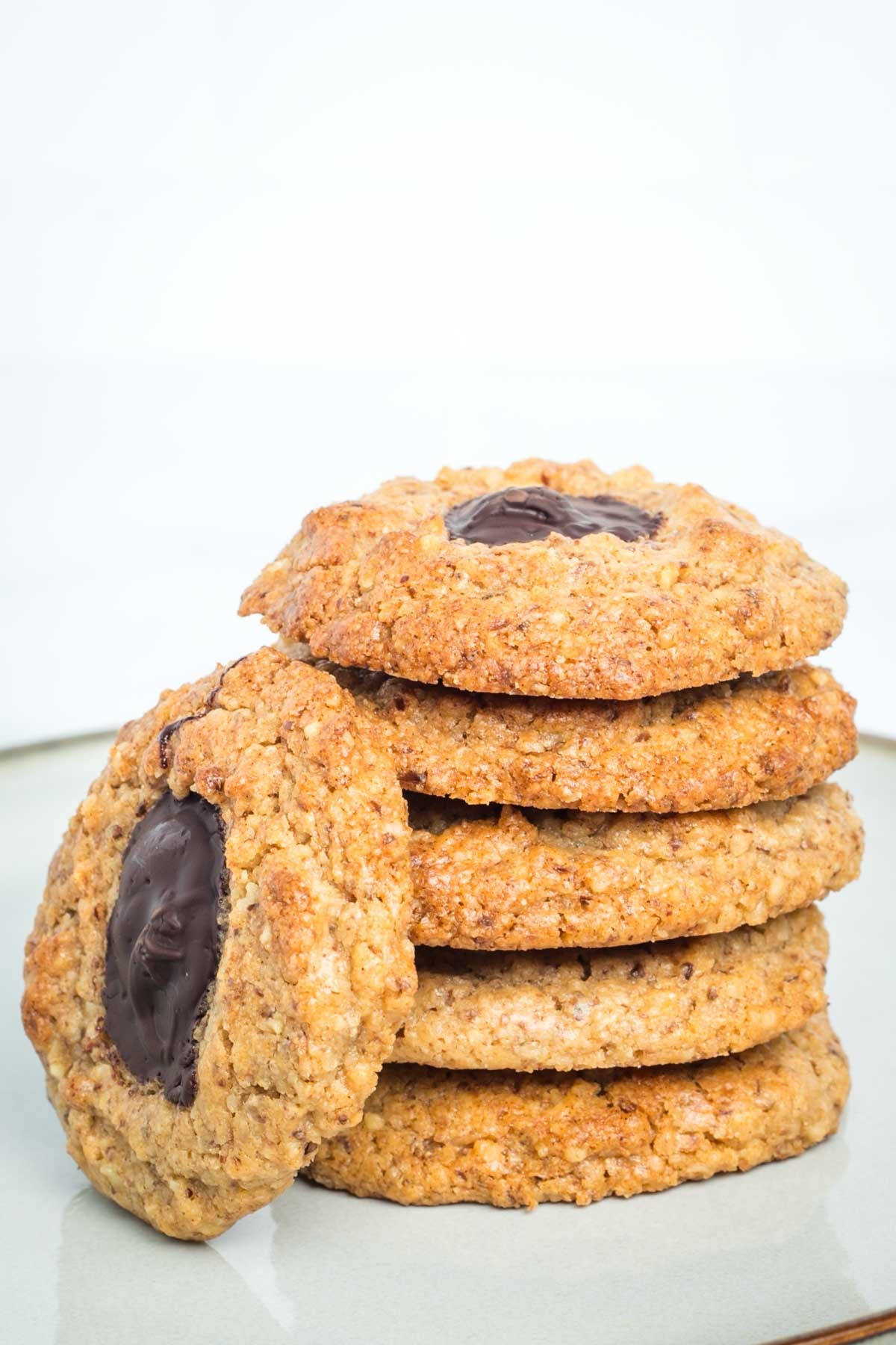 Stack of walnut thumbprint cookies, filled with chocolate and one lying on its side.