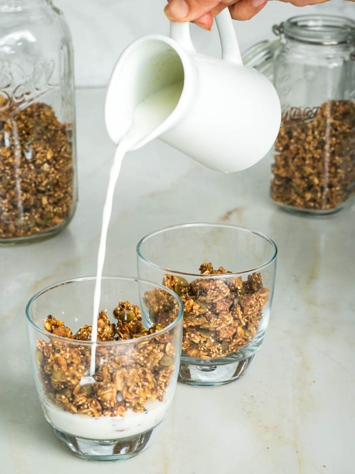 Pouring milk over pumpkin spice granola in a glass.