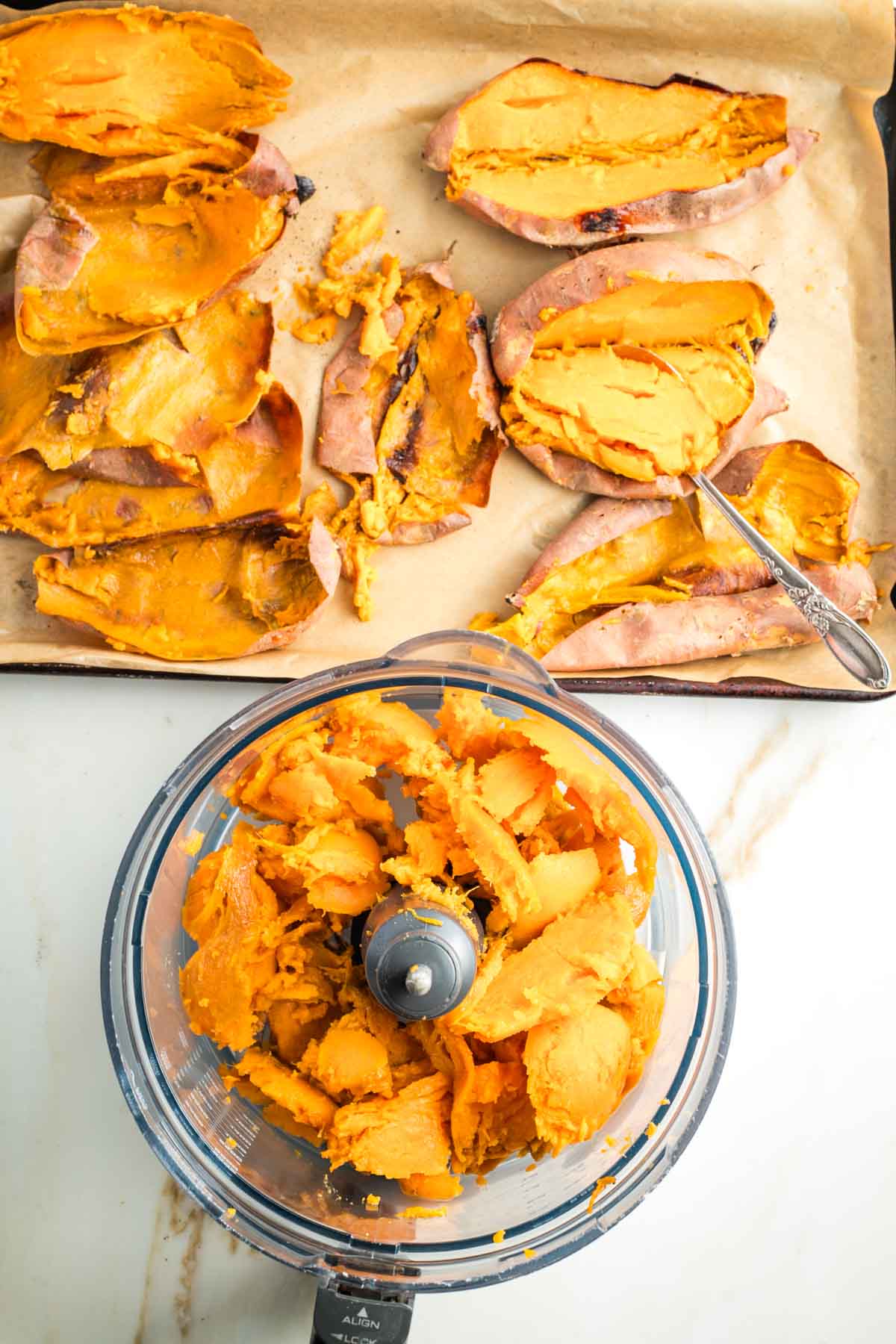 Tray of baked sweet potatoes, pulp scooped out and placed in the bowl of a food processor.