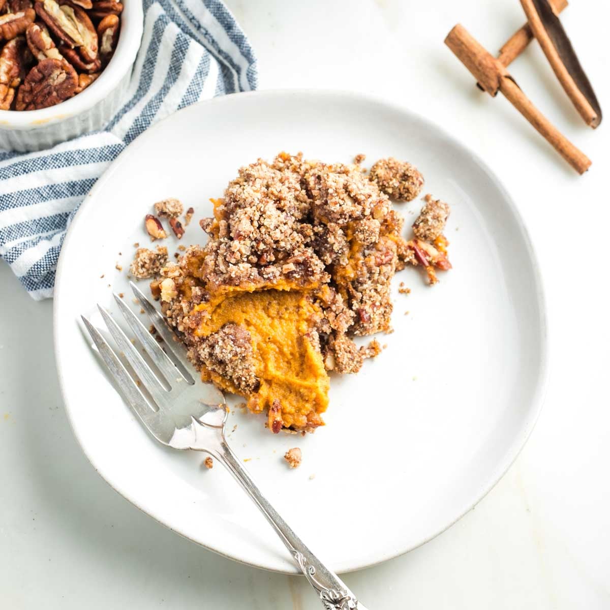 Plate and fork with serving of sweet potato casserole with pecan crumble topping, showing the orange potato mixture inside. 