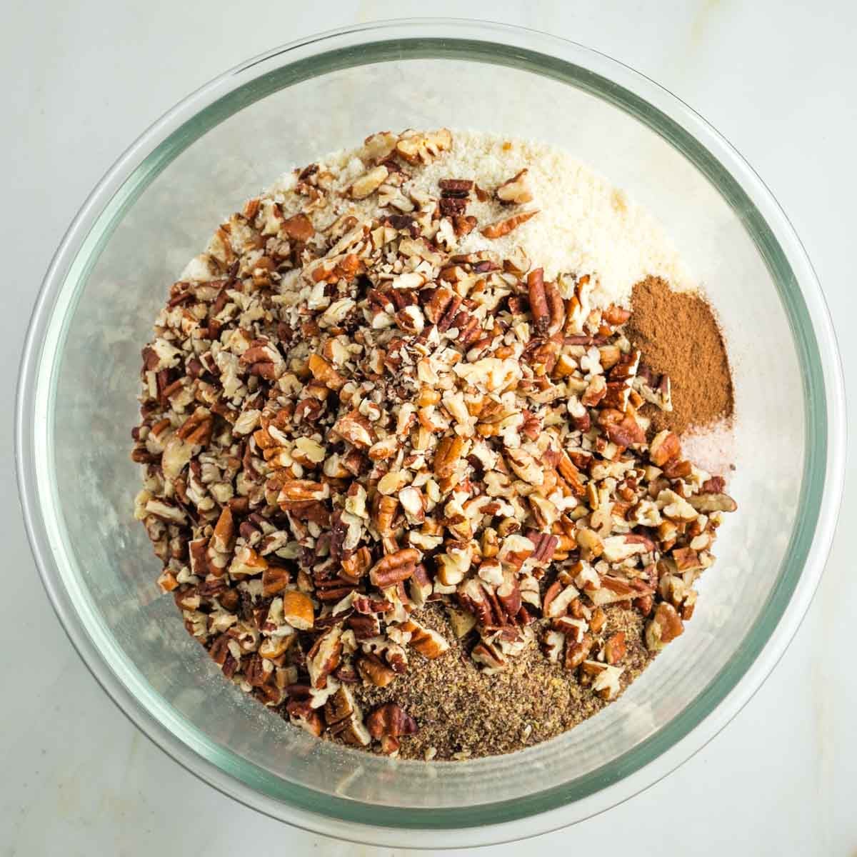 Almond flour, ground flax, chopped pecans and spices in a glass mixing bowl. 