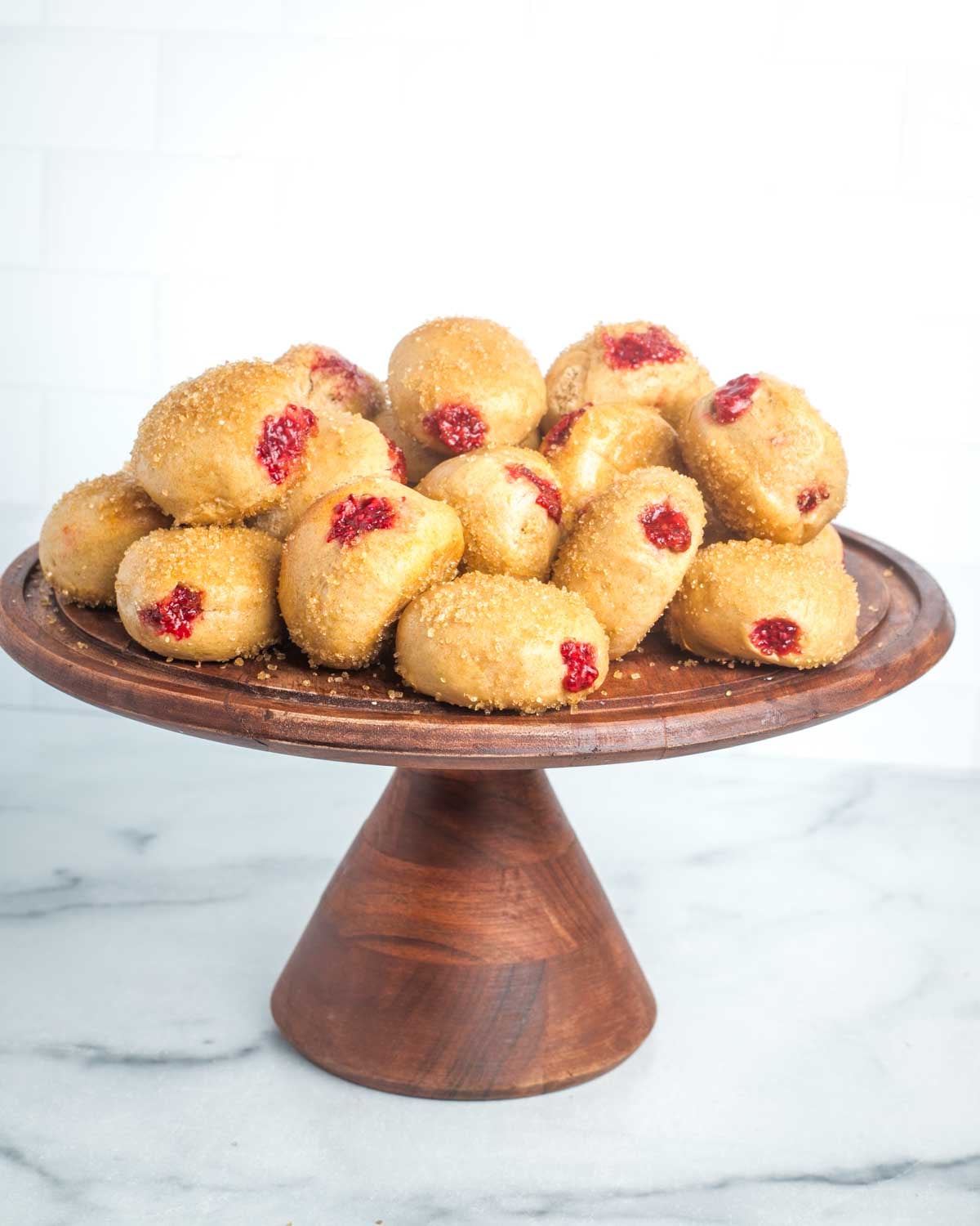 Cake stand with donuts, topped with sugar and filled with jam.