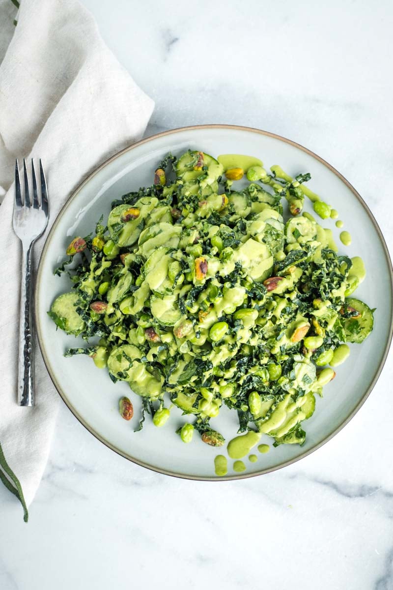 Kale, edamame and cucumber salad with creamy pistachio dressing drizzled on top. 