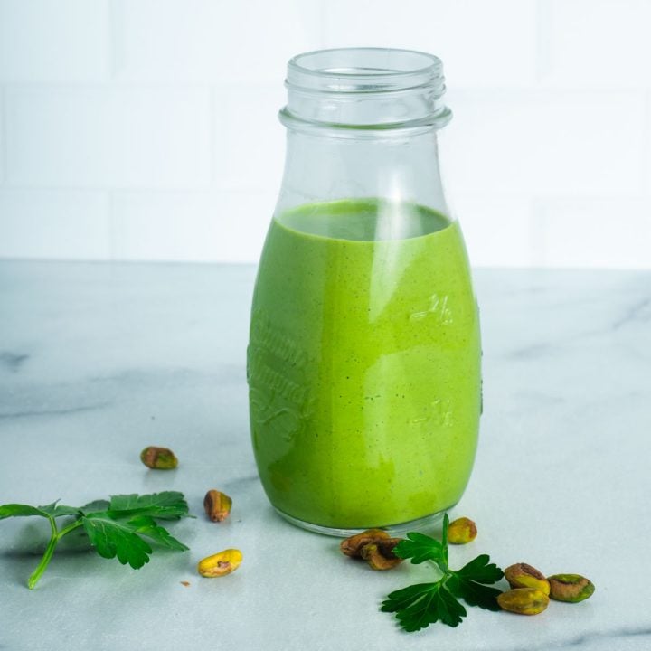 Creamy green dressing in a bottle with fresh parsley and pistachios in the foreground.