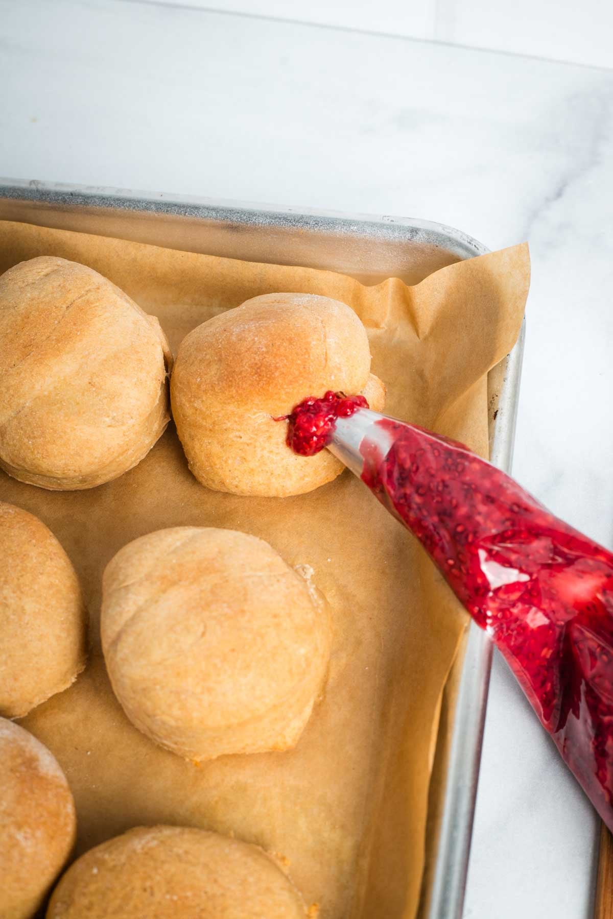 Piping bag, pushing raspberry jam into the side of a donut.