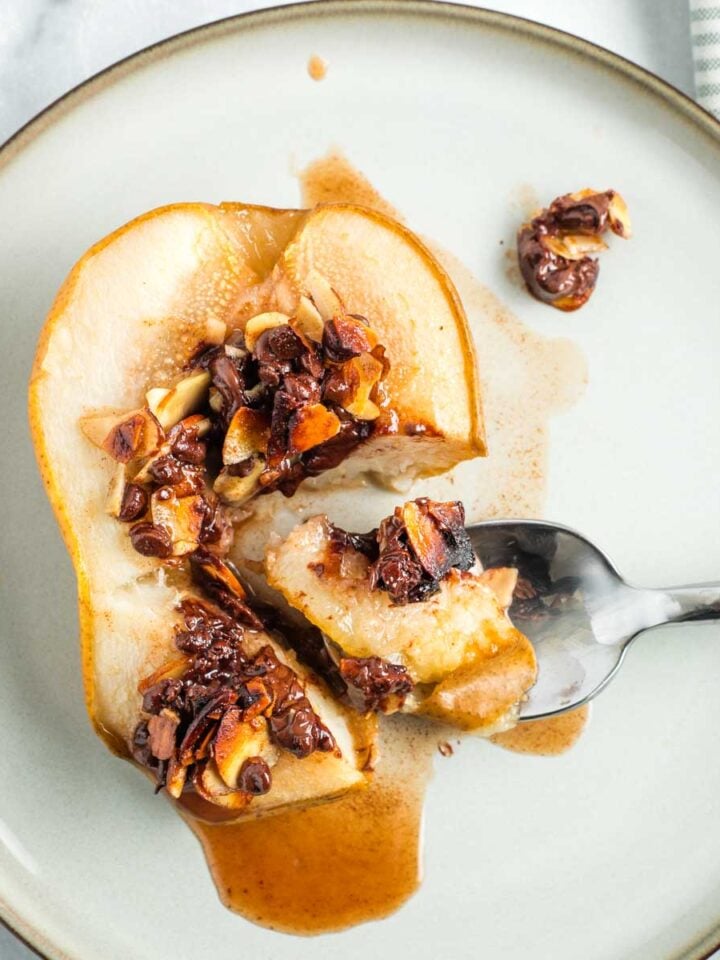 Spoonful of baked pear, showing juices oozing out and melty chocolate and golden almonds filled into center cavity.