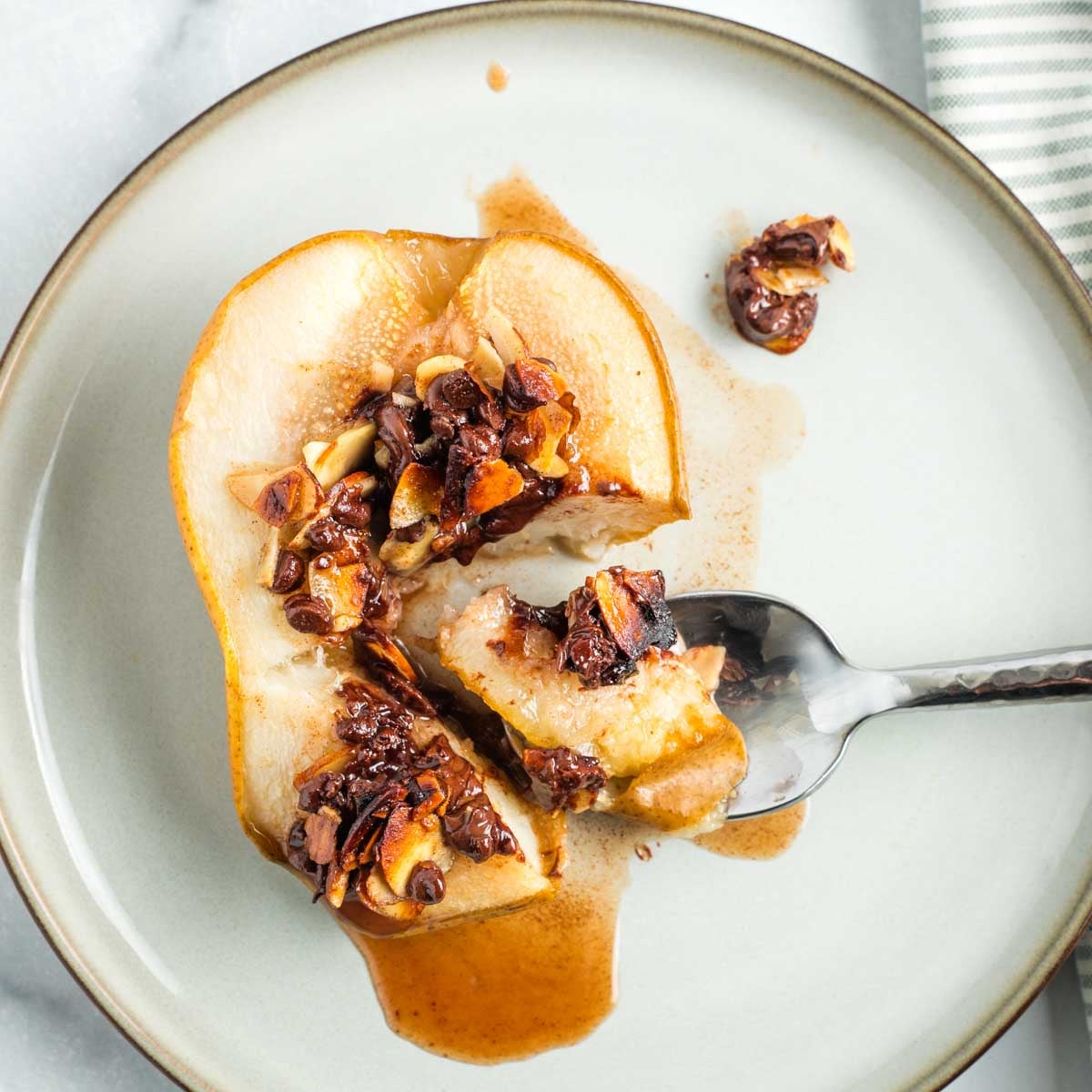Spoonful of baked pear, showing juices oozing out and melty chocolate and golden almonds filled into center cavity. 