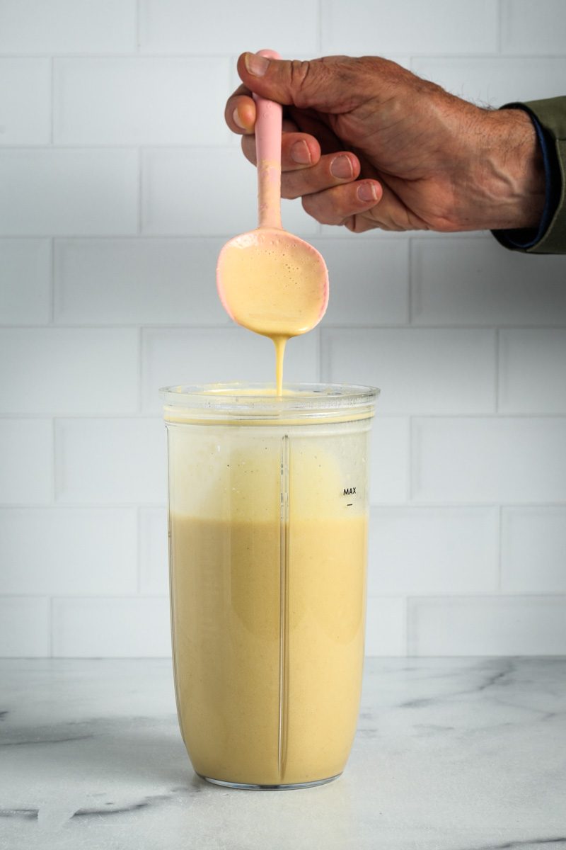 Spoon showing thickness of vegan alfredo sauce in a personalized blender cup. 