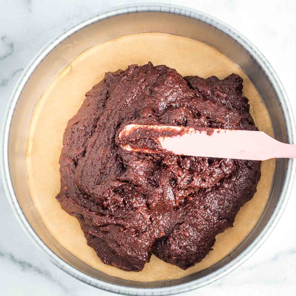 Spreading chocolate cake batter to the sides of a round cake pan.