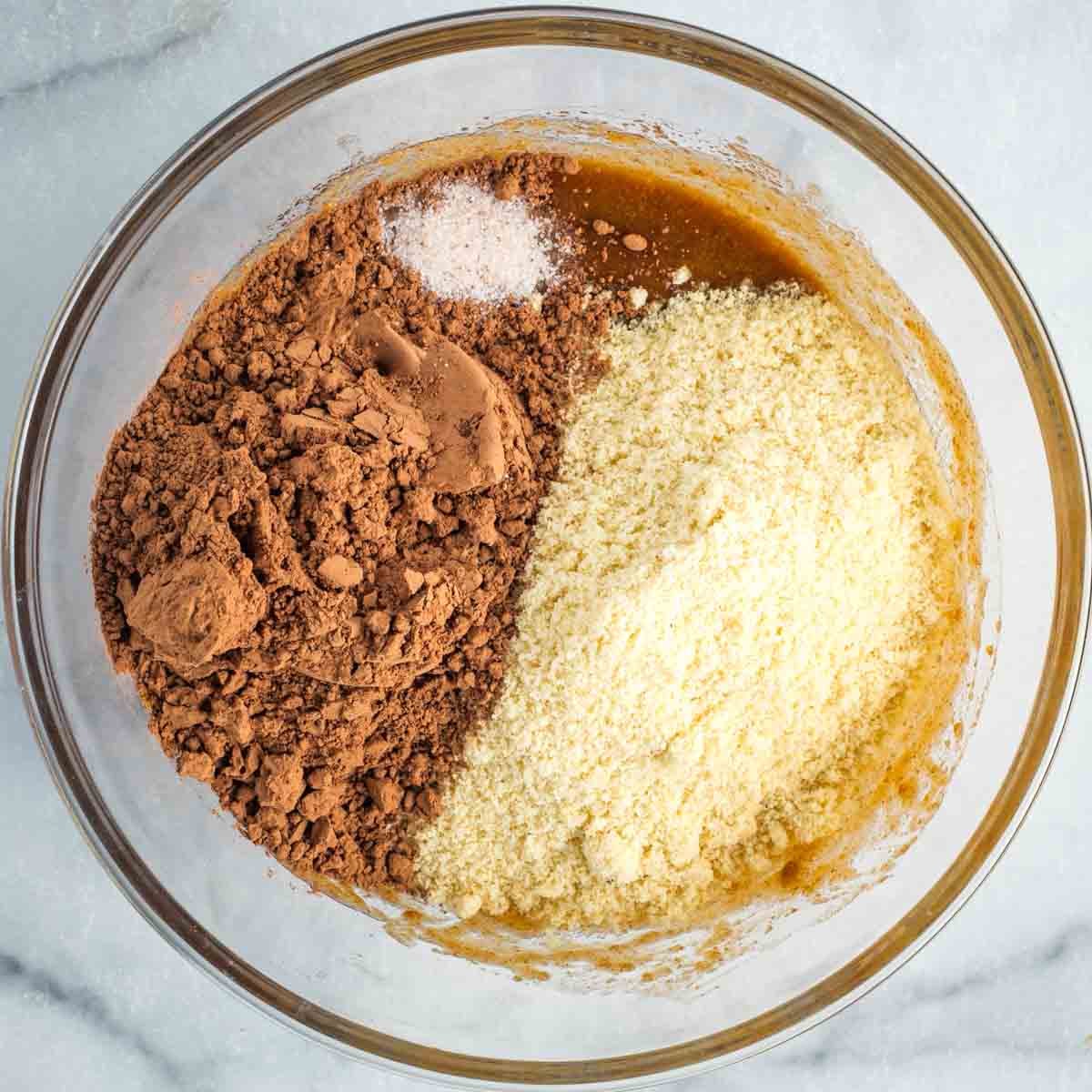 Almond flour, cacao powder and salt on top of wet cake ingredients in a medium sized mixing bowl.
