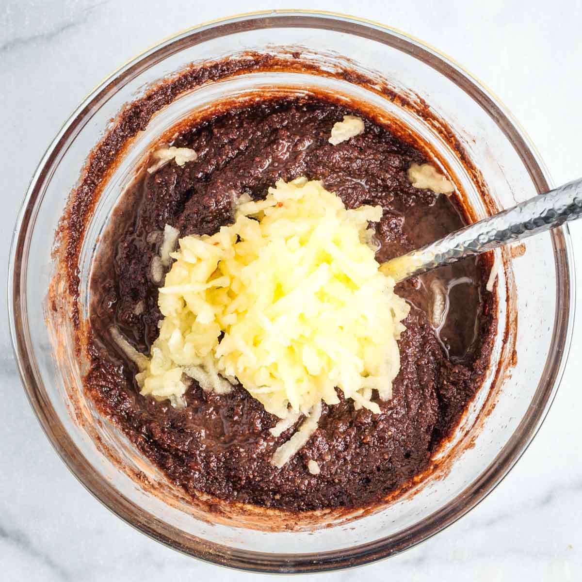 Shredded apple on top of bowl of chocolate cake batter.