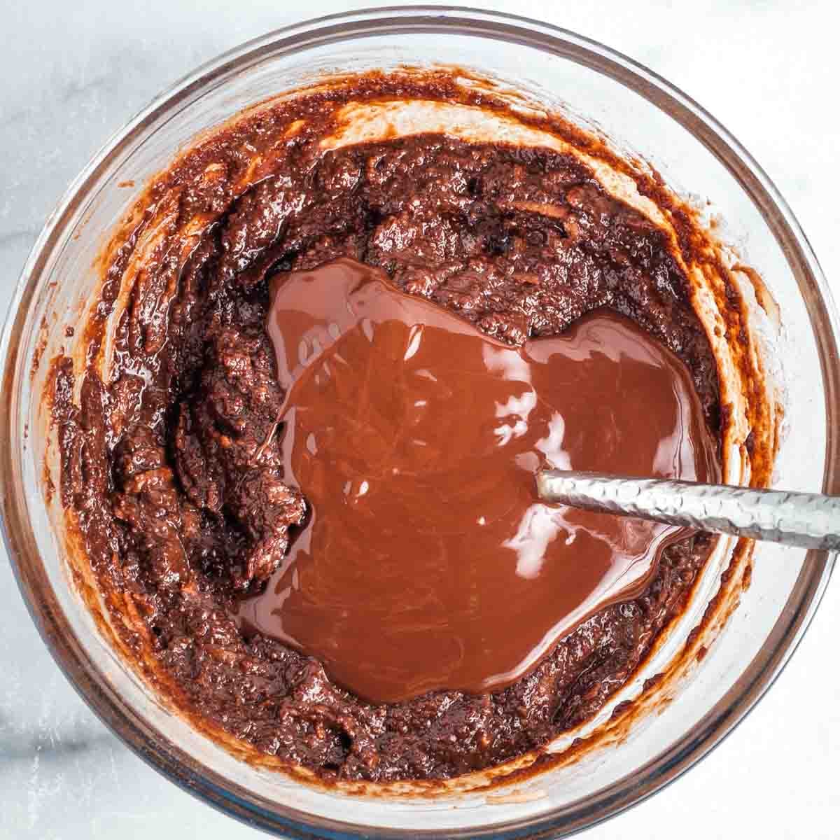 Melted dark chocolate poured on top of a bowl of chocolate cake batter.