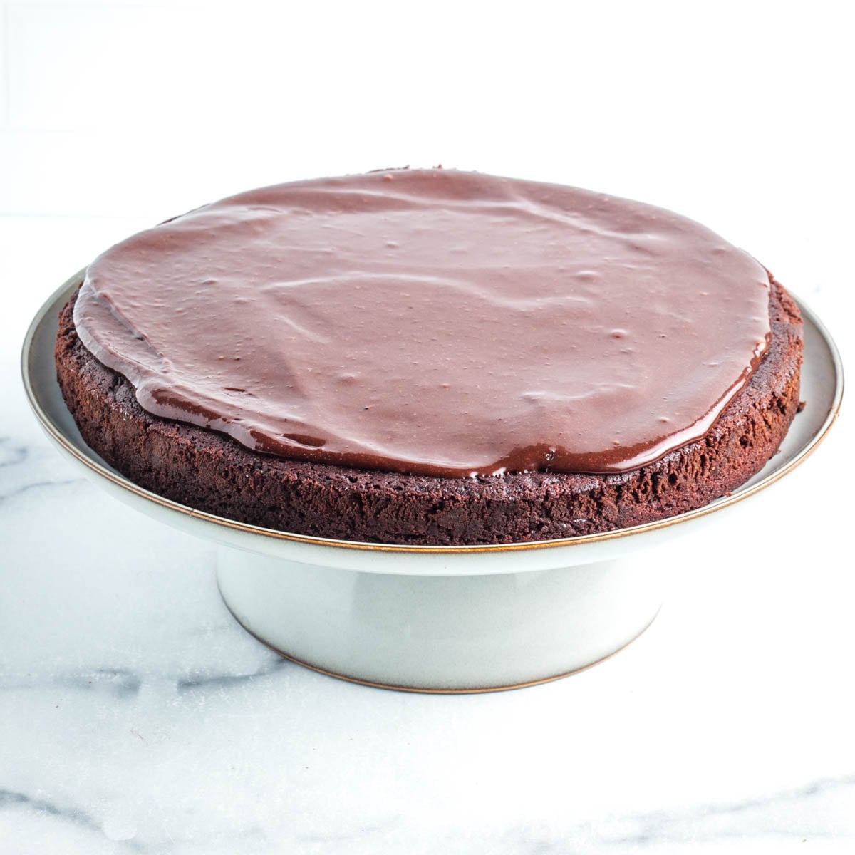 Chocolate cake with chocolate frosting on a white cake pedestal.