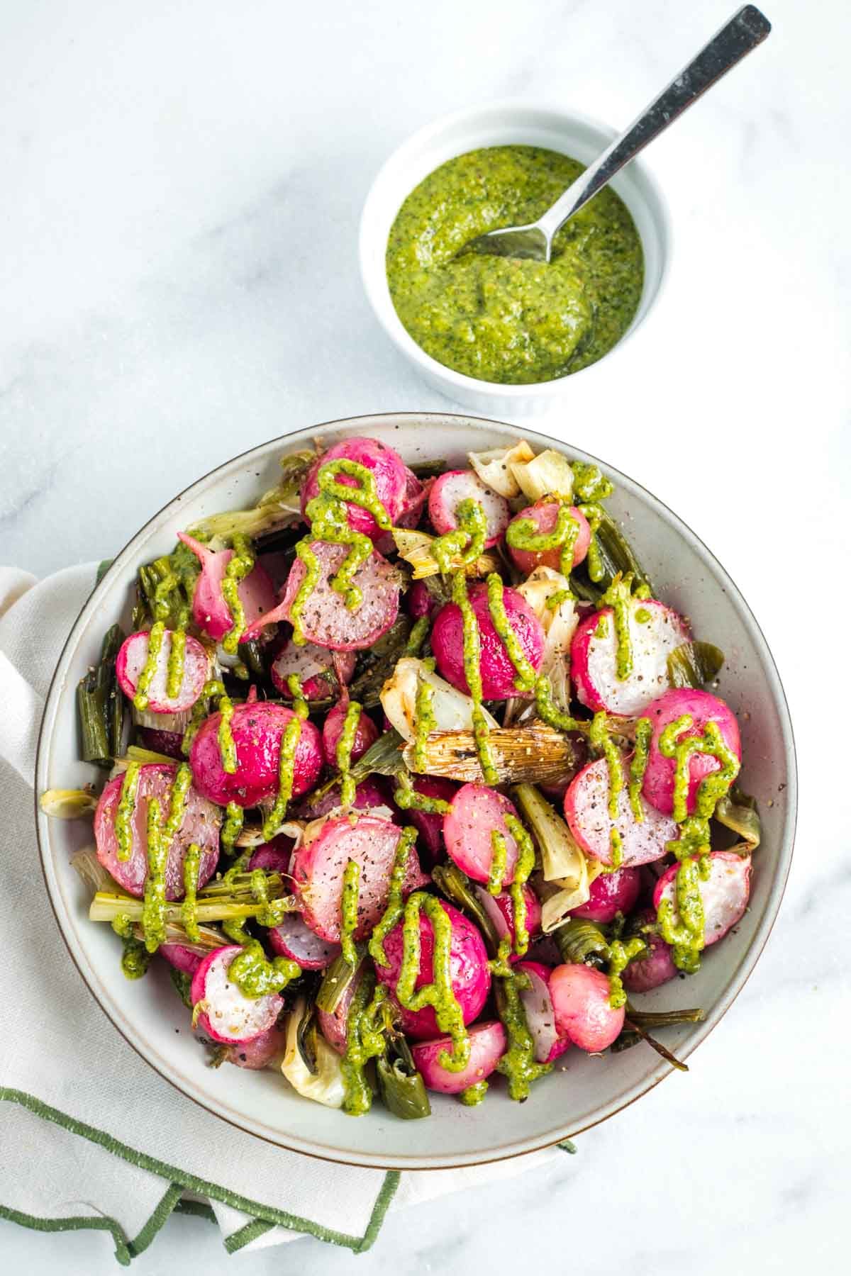 Bowl of roasted radishes and scallions, drizzled with a parsley pistachio dressing.