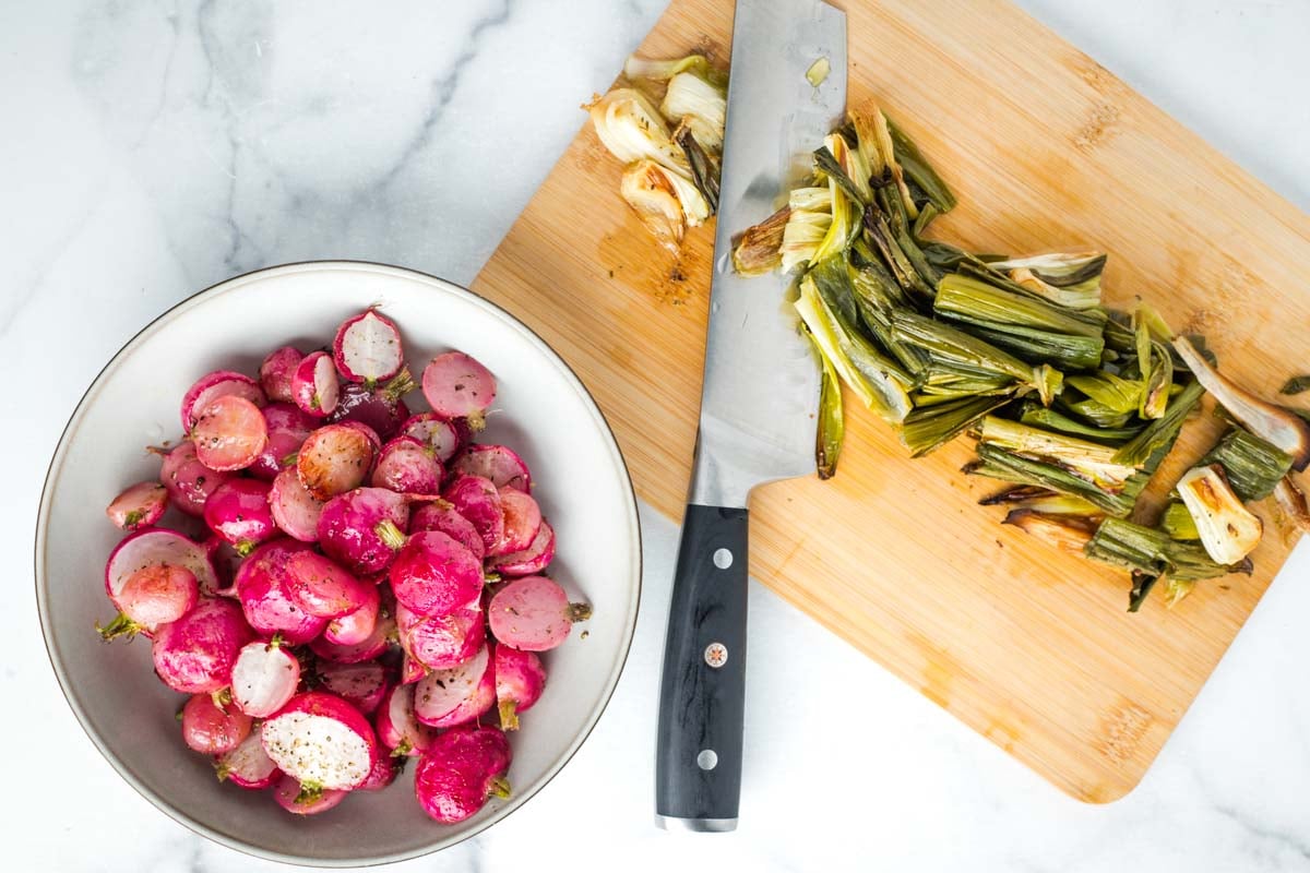 Bowl of roasted radishes and a cutting board with chopped charred scallions.