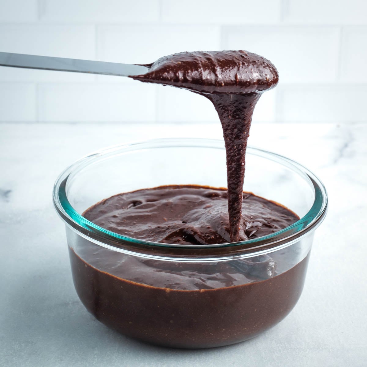 Spatula with chocolate frosting dripping back into the bowl. 
