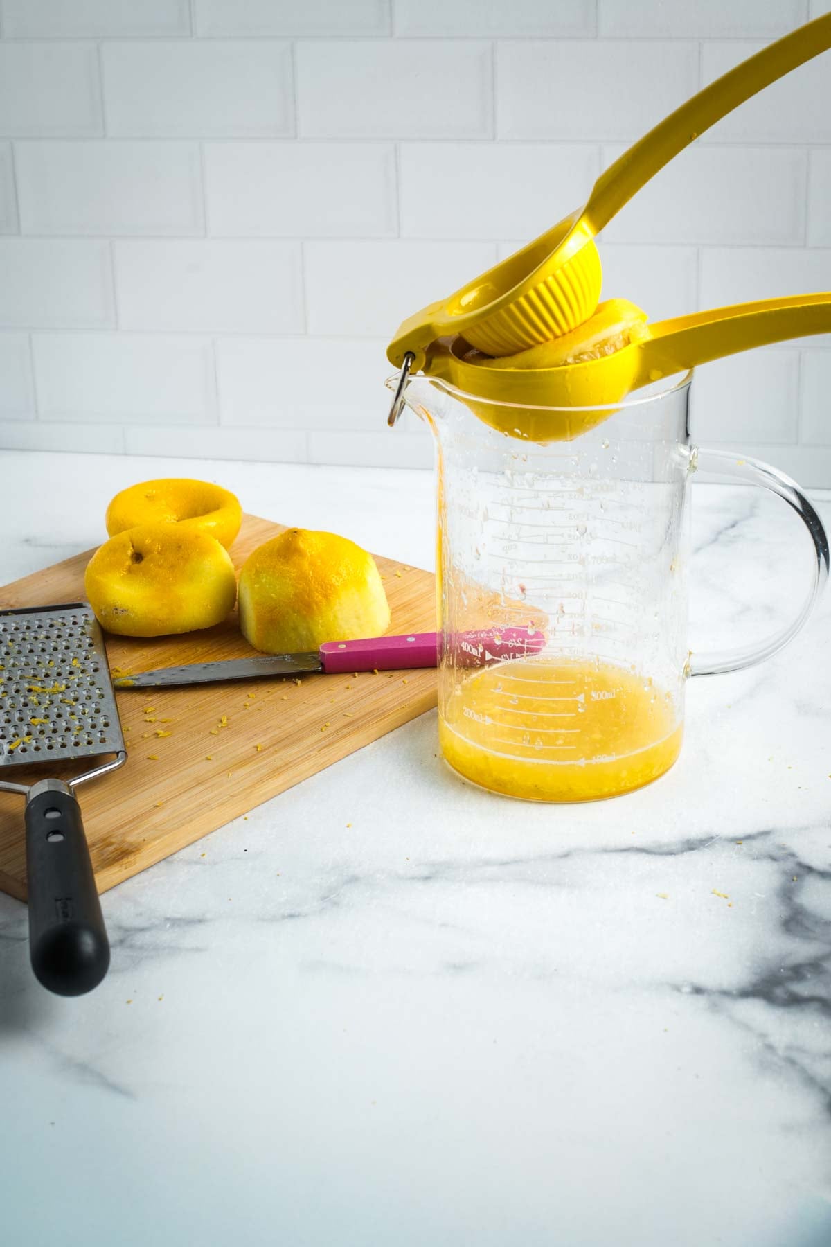 Juicing a lemon over a small glass pitcher that has the zest already in it. 
