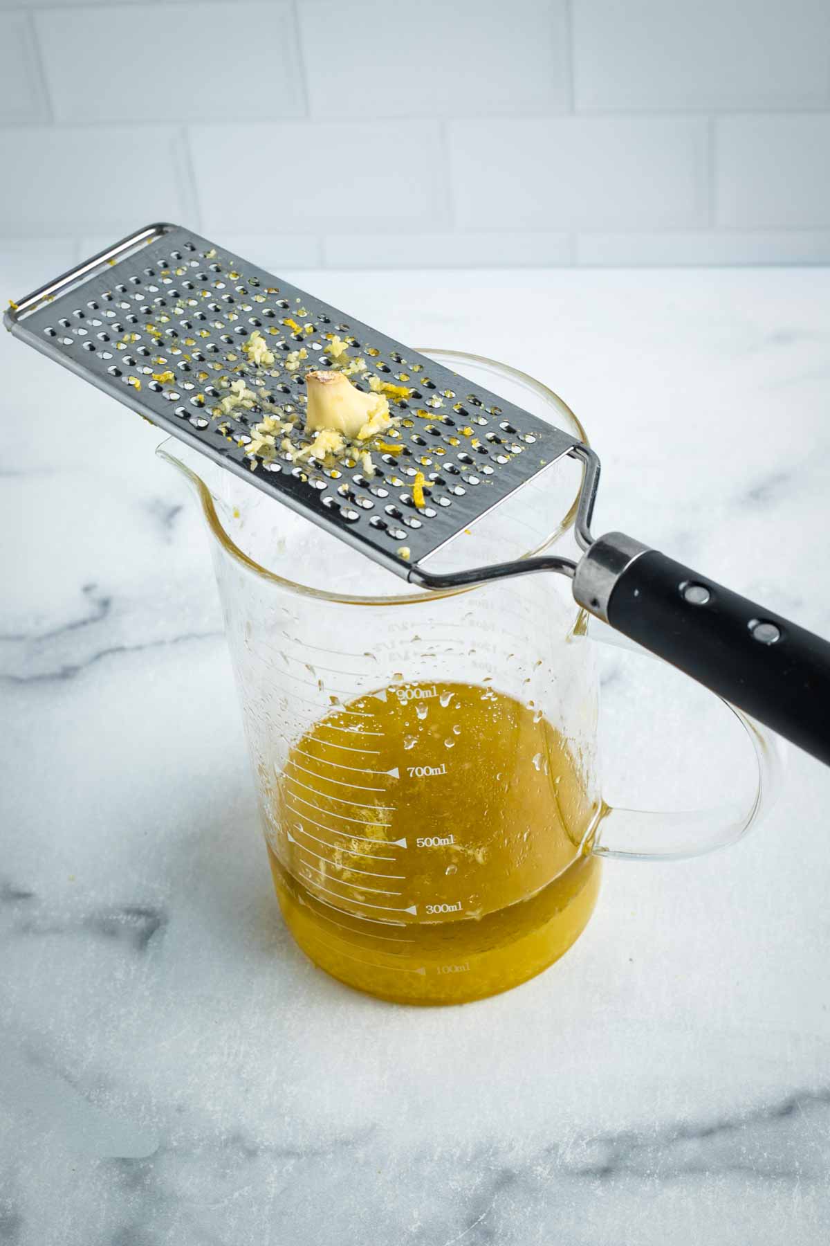 Finely grating garlic over a small glass pitcher of lemon zest and juice. 
