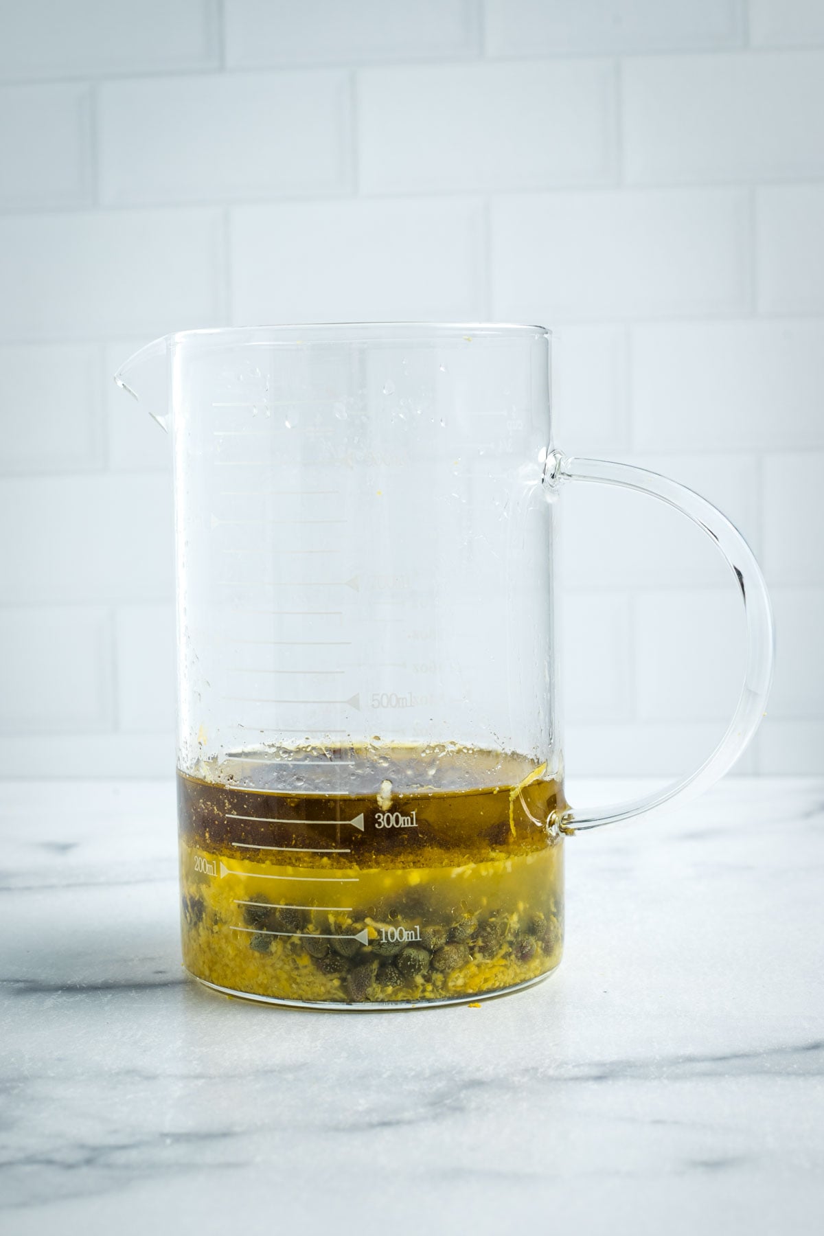 Small glass pitcher with ingredients to make lemon dill dressing with capers and dates.