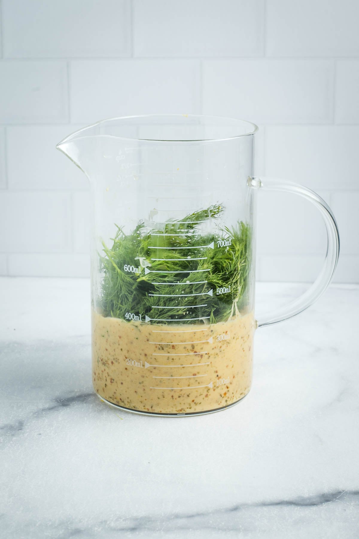Fresh dill piled onto a creamy lemon dressing in a small glass pitcher. 