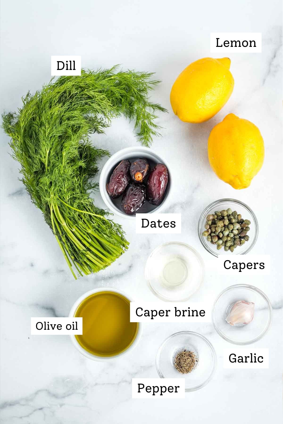 Labeled ingredients for lemon dill dressing: dill, lemon, dates, capers, caper brine, olive oil, garlic and black pepper. 