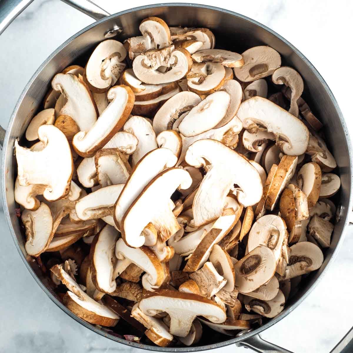 Sliced shitake and portobello mushrooms in a soup pot. 