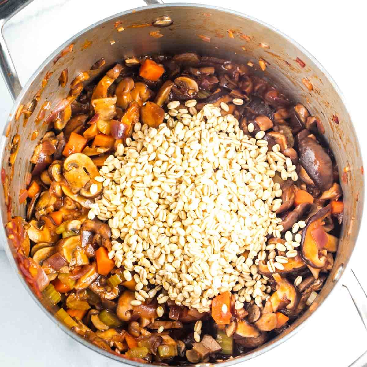 Dried pearl barley on top of sauteed veggies in tomato sauce in a soup pot.