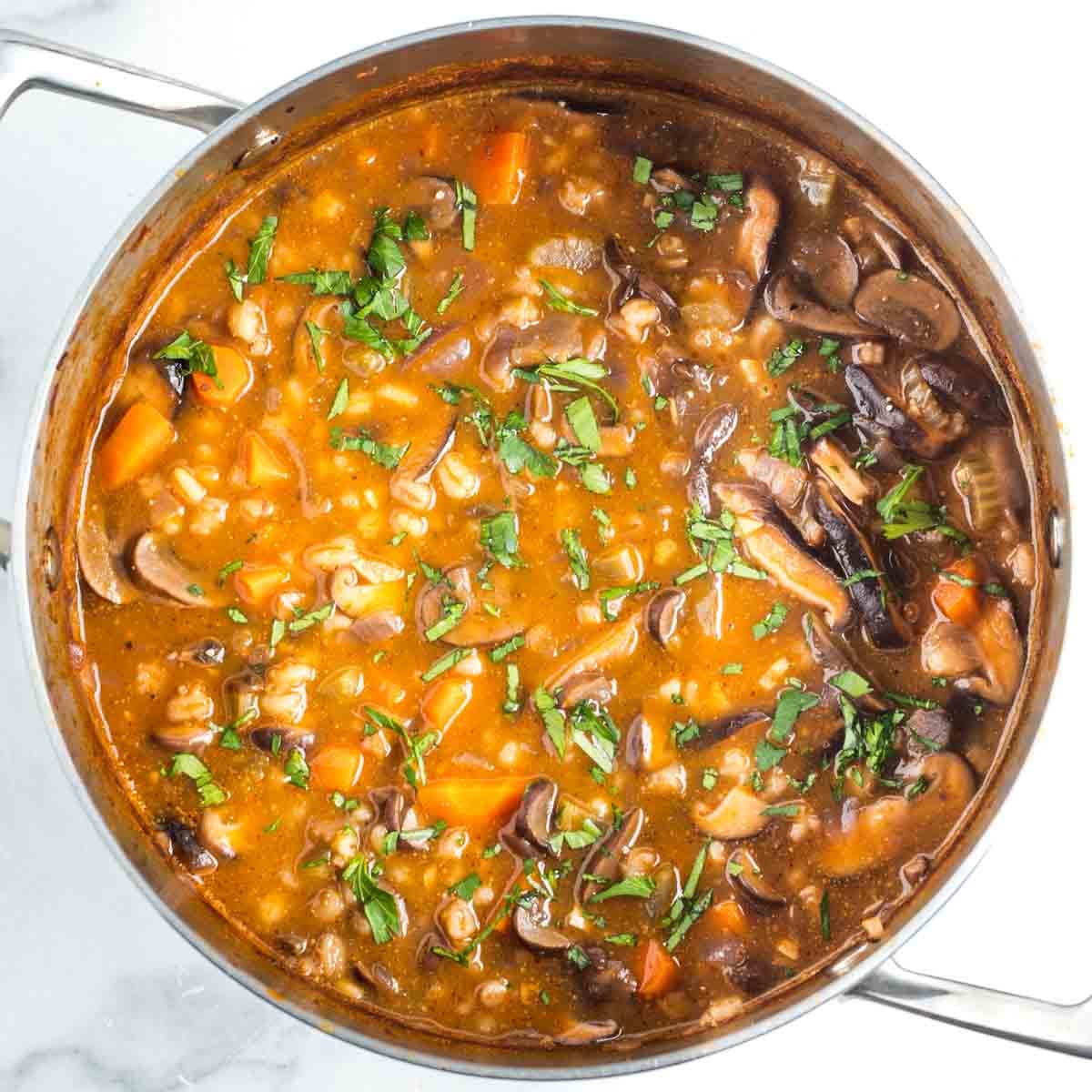 Mushroom barley soup in a tomato broth, with chunks of carrots, sprinkled with fresh herbs.