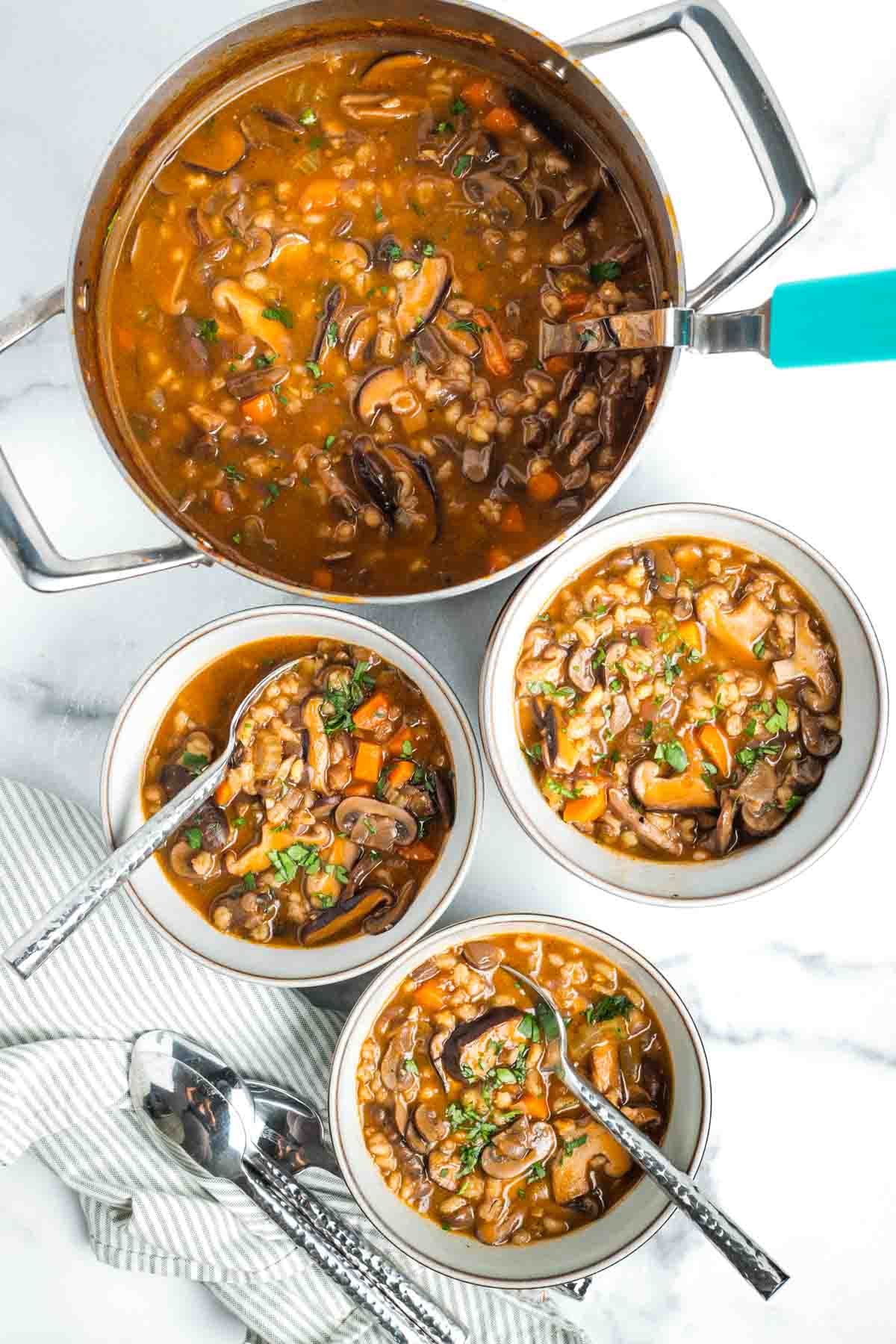 Three bowls of chunky mushroom barley soup and a pot full with ladle. 