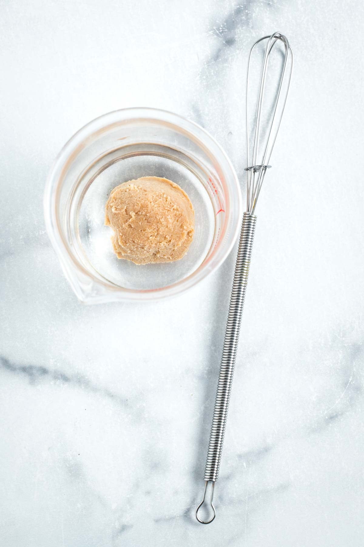 Miso paste in a small glass of water with a whisk on the side. 