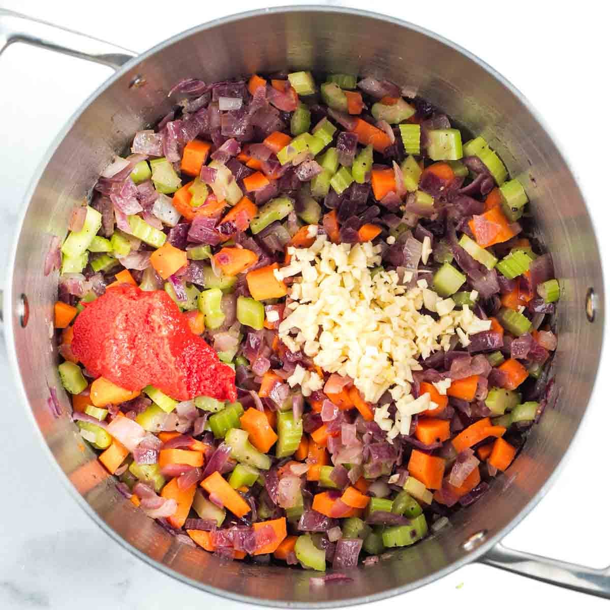 Sauteed carrot, onion and celery in a soup pot with tomato paste and garlic added on top. 