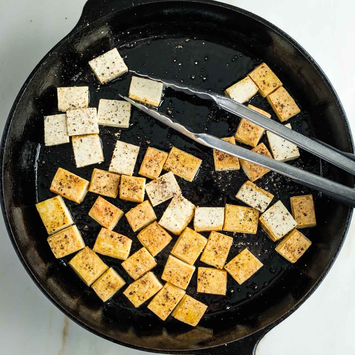 Turning cubes of tofu over in a skillet as they're golden brown.