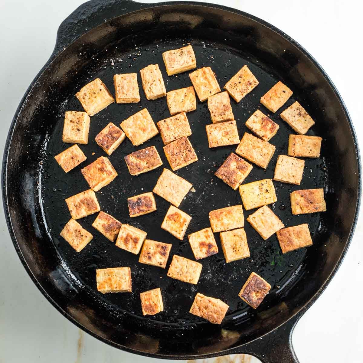Cast iron skillet with browned cubes of tofu.