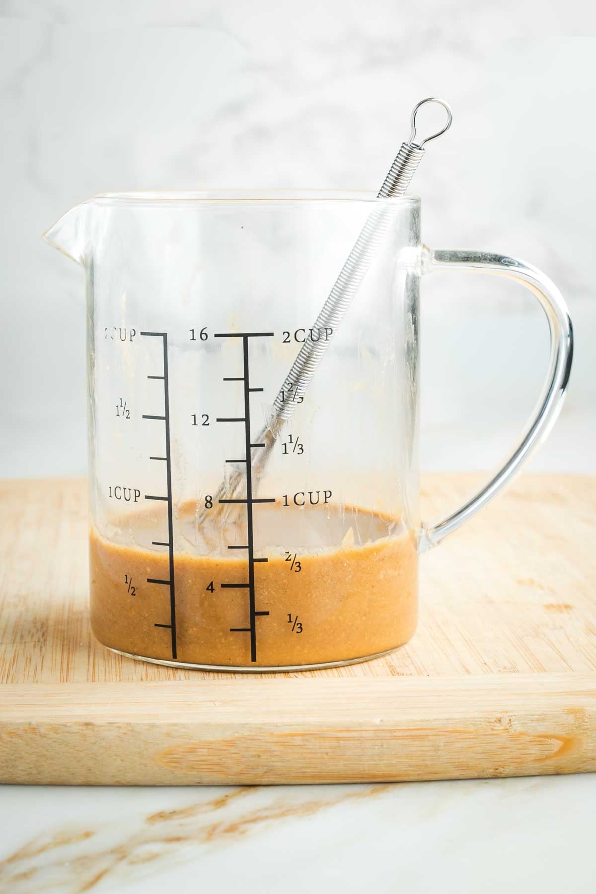 Glass pitcher with measuring marks on the side, a whisk making ginger sesame dressing.