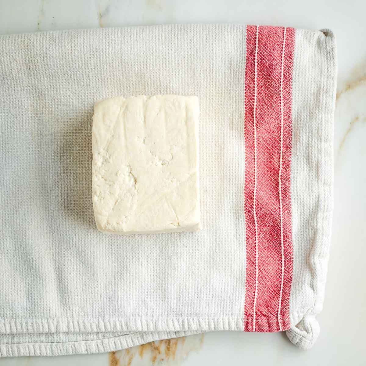 Block of tofu on a white tea towel with red stripe.